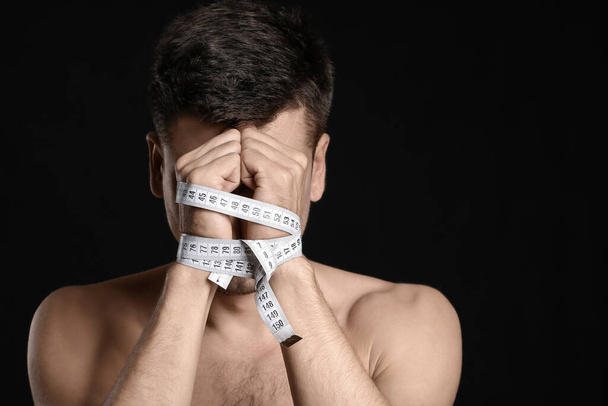 Sick man with measuring tape on dark background. Concept of anorexia - Φωτογραφία, εικόνα