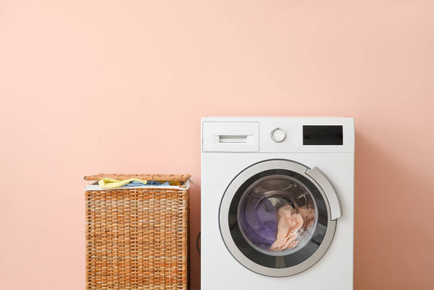 Wasmachine en mand met was in de buurt van kleur muur - Foto, afbeelding