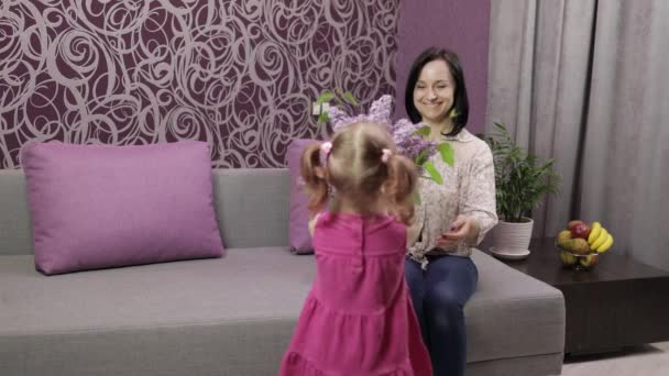 Kleine Tochter gratuliert ihrer Mutter mit fliederfarbenem Blumenstrauß - Filmmaterial, Video