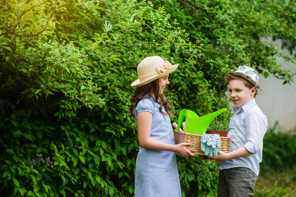 Usmívající se roztomilá dívka a blonďatý chlapec zahradník drží koš a zahradnické nářadí v zahradě za slunečného dne. Letní aktivity - Fotografie, Obrázek