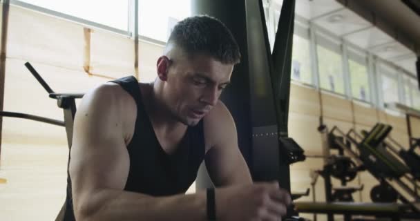 Portrait of professional muscular athletic man bodybuilder in shorts is sitting on bench in closed gym - Footage, Video
