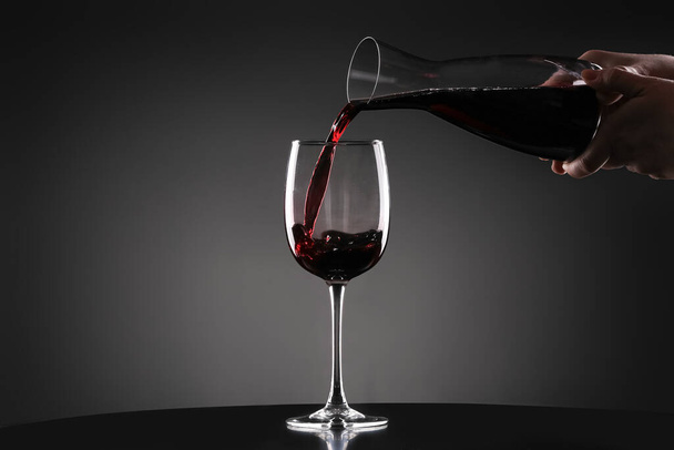 暗い背景にデカンターからガラスにおいしいワインを注ぐ - 写真・画像