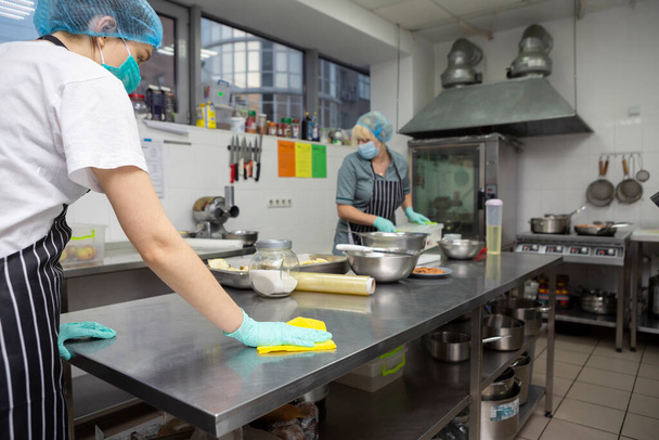 Mujer con máscara protectora y guantes desinfectando mesa de cocina
 - Foto, Imagen