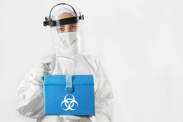 Isolated young woman in medical uniform and mask holding a first aid kit with biohazard sign on. Healthcare and medical concept. - Photo, Image