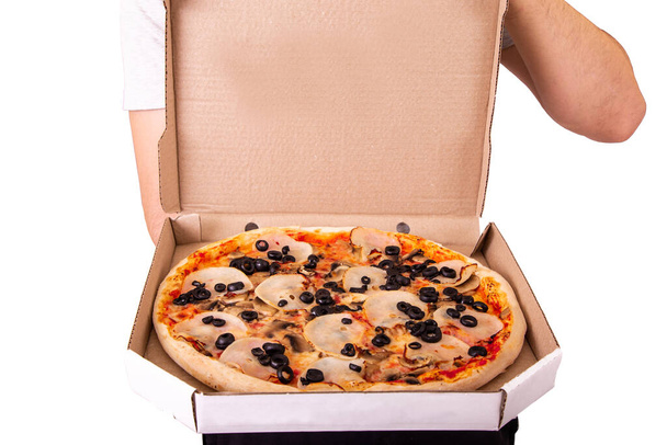A young man opens the cardboard box, pizza delivery service. Delicious fresh pizza with ham, mozzarella, mushrooms and olives, isolated on white background - Photo, Image