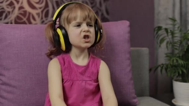 Malá holčička ve sluchátkách si užívá poslouchání hudby. Tanec na gauči doma - Záběry, video