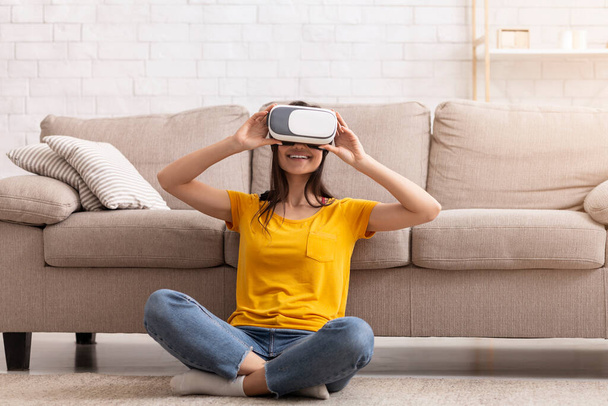 Millennial girl in virtual reality headset exploring cyberspace, playing interactive video game at home - Foto, Bild