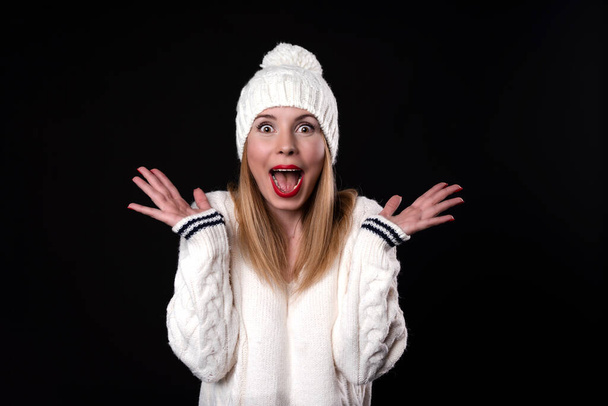 Image of surprised woman wearing glasses and dressed in white sweater over black background. Look at camera. - Fotografie, Obrázek