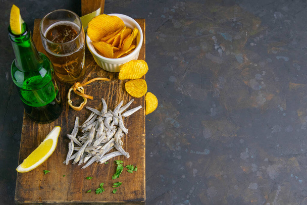 Anchois salés séchés avec bière, citron et croustilles sur une planche de bois foncé. Snack sur le poisson avec de la bière. Top vues avec espace libre
. - Photo, image