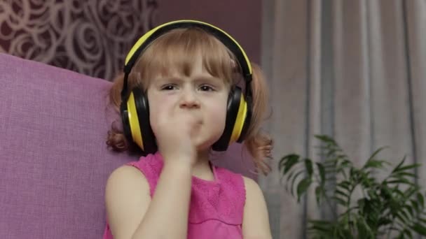Kleines Mädchen mit Kopfhörern, das Musik hört. Zu Hause auf dem Sofa tanzen - Filmmaterial, Video