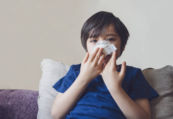 Unhealthy kid with dry skin blowing nose into tissue, Child suffering from running nose or sneezing, A boy catches a cold when season change, childhood wiping nose with tissue - 写真・画像