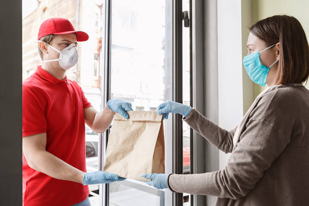 Kurier in Schutzmaske und Handschuhen gibt Paket sorgfältig an Kunden weiter - Foto, Bild