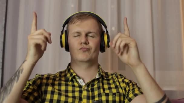 Man sitting on the sofa listens music from wireless headphones and dances - Imágenes, Vídeo