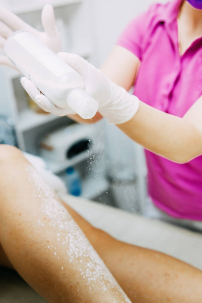 the hair removal master works with the legs using sugar waxing, sprinkles talcum powder on the client's legs. - 写真・画像