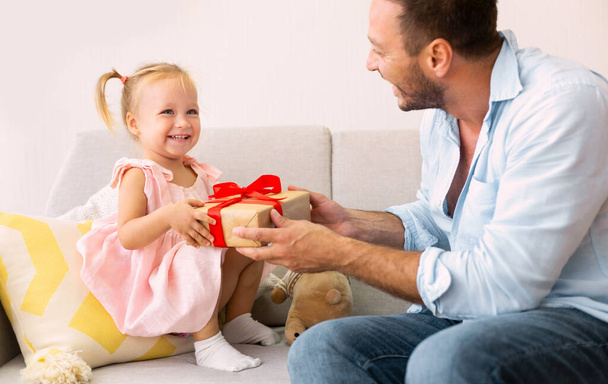 podekscytowana dziewczyna trzyma jej prezent siedzi z tatą - Zdjęcie, obraz