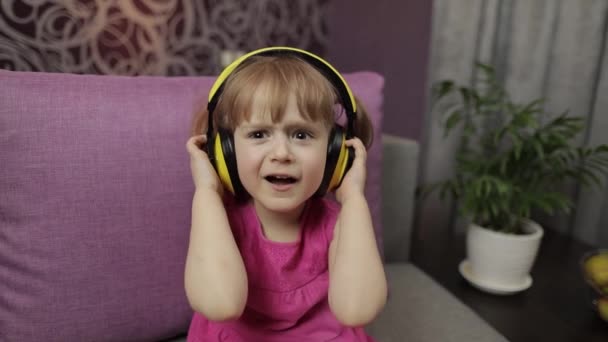 Little child girl in headphones enjoying listen music. Dancing on sofa at home - Footage, Video