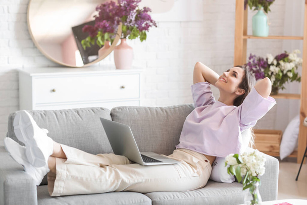 Όμορφη νεαρή γυναίκα με φορητό υπολογιστή χαλαρώνοντας στο σπίτι - Φωτογραφία, εικόνα