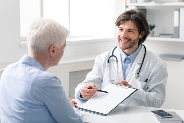 Friendly geriatrician explaining prescription for senior patient - Foto, afbeelding