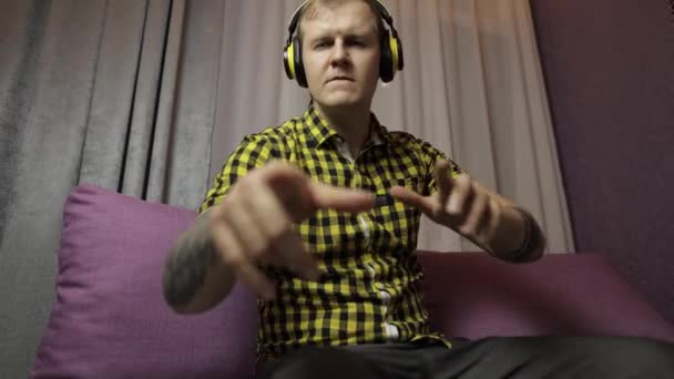 Man sitting on the sofa listens music from wireless headphones and dances - Materiał filmowy, wideo
