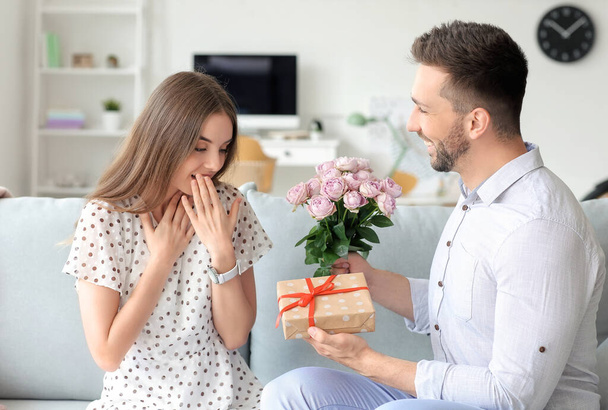 Mies antaa kukkakimpun ja lahjan tyttöystävälleen kotona
 - Valokuva, kuva