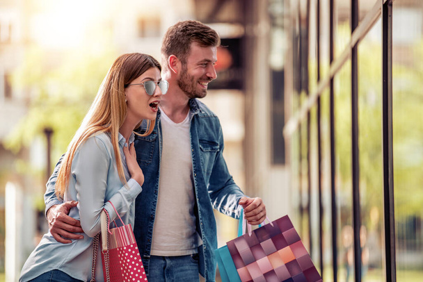 Glückliches schönes junges Paar hält Einkaufstüten in der Hand, schaut in die Vitrine und lächelt. - Foto, Bild