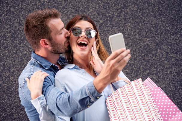 Couple heureux avec sacs à provisions prendre selfie avec téléphone intelligent. - Photo, image