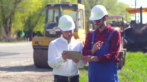 Manager of the repair works and worker on road. Road manager shows worker road construction plan on a tablet. Road repair concept - Footage, Video