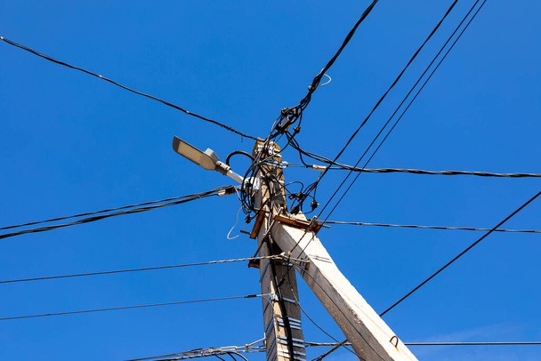 Ένας τσιμεντένιος ηλεκτρικός στύλος με λάμπα του δρόμου και πολλά καλώδια σε έναν γαλάζιο ουρανό - Φωτογραφία, εικόνα