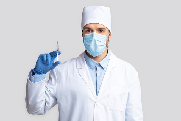 Уверенный в себе врач в защитной одежде держит шприц
 - Фото, изображение