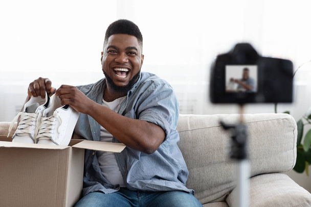 Radosny czarny człowiek blogger nagrywanie Unboxing wideo z nowej pary butów - Zdjęcie, obraz