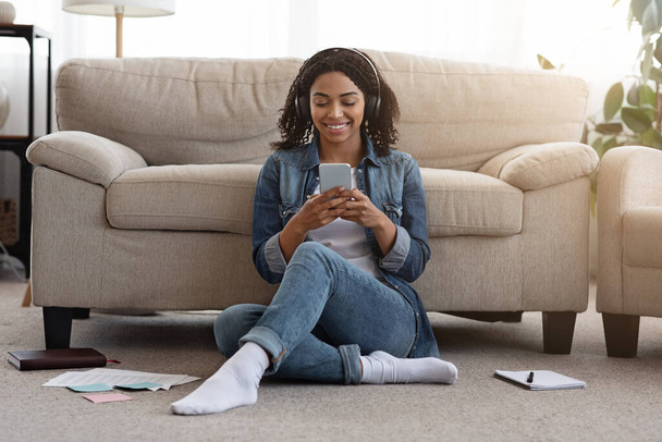 Černá dívka poslouchá oblíbenou píseň na Smartphone při studiu doma - Fotografie, Obrázek