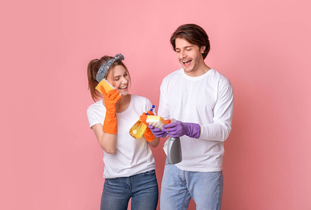 Verrückte Reinigung. Fröhliches Paar benutzt Schwämme wie Handys und hat Spaß beim Aufräumen - Foto, Bild