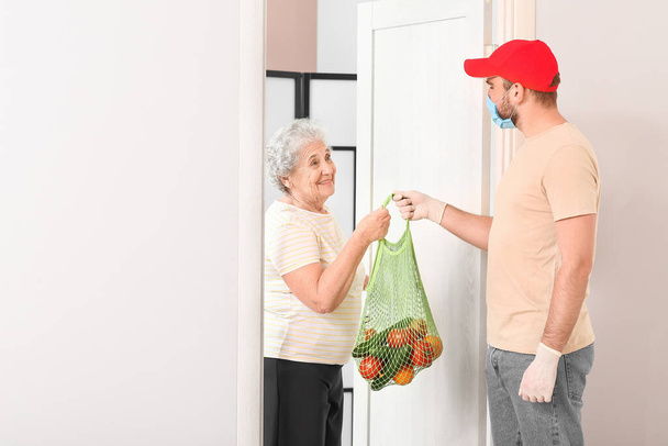 Starsza kobieta otrzymuje jedzenie od kuriera w domu. Pojęcie epidemii - Zdjęcie, obraz
