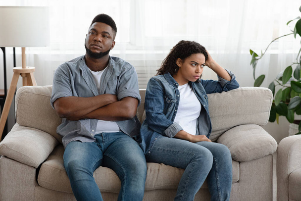Cuarentena Quarrels. Pareja afroamericana ignorándose mutuamente después de discutir en casa, sentada en diferentes lados del sofá
 - Foto, imagen