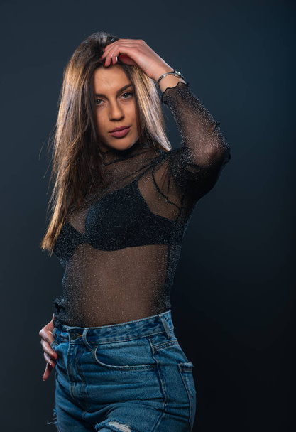Sensueel portret van een aantrekkelijk vrouwelijk model poserend in jeans en sprankelend transparant shirt - Foto, afbeelding
