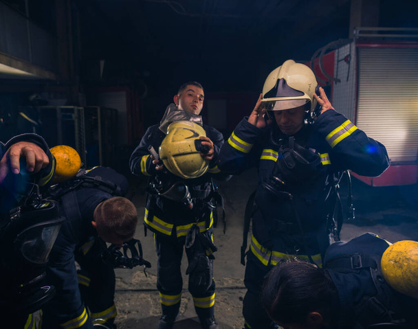 Grupo de bomberos de pie dentro de la brigada de bomberos con casco y uniforme de protección - Foto, imagen