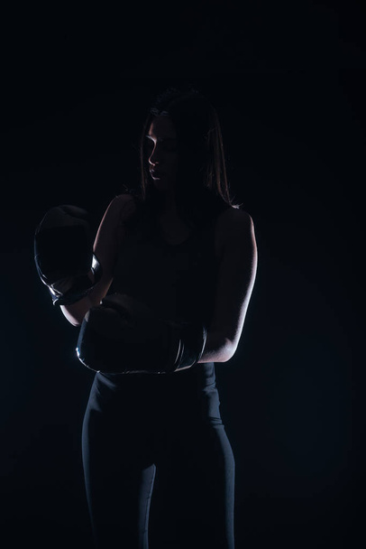 Silhouet portret van een sexy fit vrouw poseren in donker contrast met bokshandschoenen - Foto, afbeelding