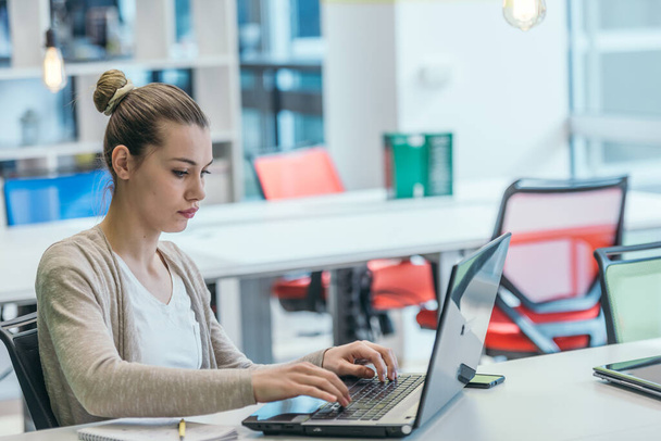 Blonde Geschäftsfrau arbeitet an ihrem PC, während sie in einem überfüllten modernen Büro sitzt. - Foto, Bild