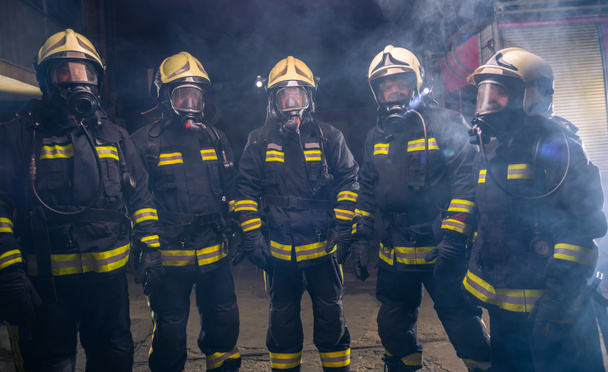 Yangın söndürücünün dumanının ortasında bir grup itfaiyecinin portresi. - Fotoğraf, Görsel