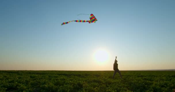 Ein Junge spielt bei Sonnenuntergang mit einem Drachen am Himmel. 4K - Filmmaterial, Video