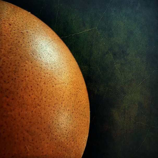 A closeup shot of an orange round object on a dark green background - Фото, изображение