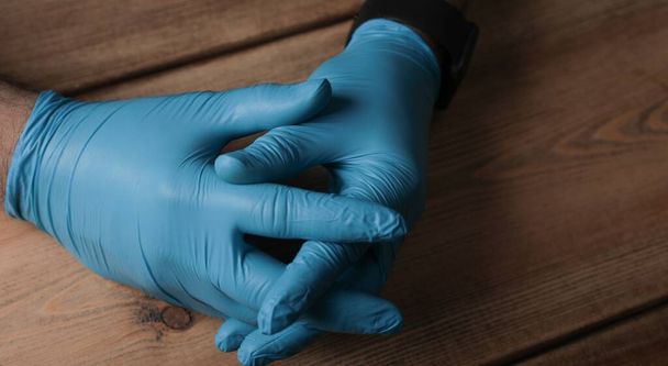 A high angle shot of a man's hands in medical blue gloves on a wooden background - Foto, afbeelding