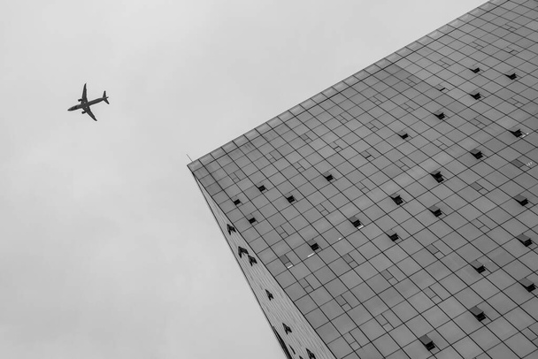 Uma vista de baixo ângulo para um edifício e um avião voando perto dele no céu
 - Foto, Imagem