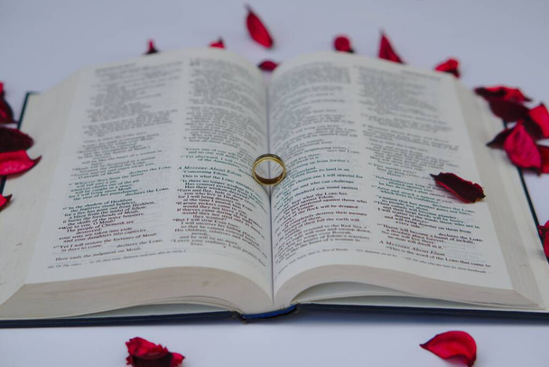 A golden ring on a book with red rose petals - Zdjęcie, obraz