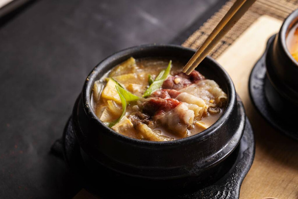A high angle shot of a bowl of delicious soup and bacon and chopsticks on a black table - Фото, зображення