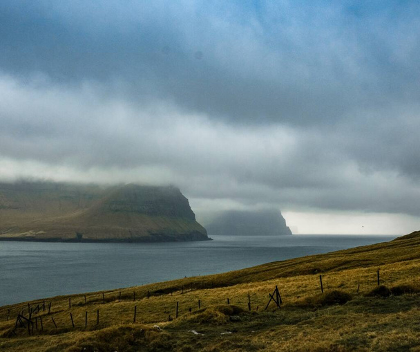 The mesmerizing view of the cliffs on the shore of a calm lake on a cloudy day in Faroe islands - Φωτογραφία, εικόνα