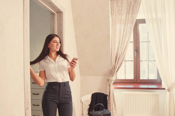 Positive successful businesswoman in a bright hotel room with a phone in her hand. - Fotoğraf, Görsel