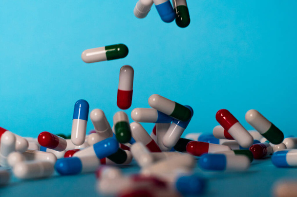 Barevné pilulky padají na modré pozadí. Léky padají. Červené, zelené, modré a bílé pilulky na modrém stole - Fotografie, Obrázek