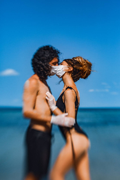 young couple hugging and kissing through the face masks on the beach - Foto, immagini