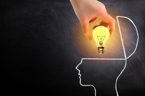 ビジネスアイデアコンセプト:手を保持電球の照明が成長し、黒板に脳の白いチョークドアを入れて. - 写真・画像